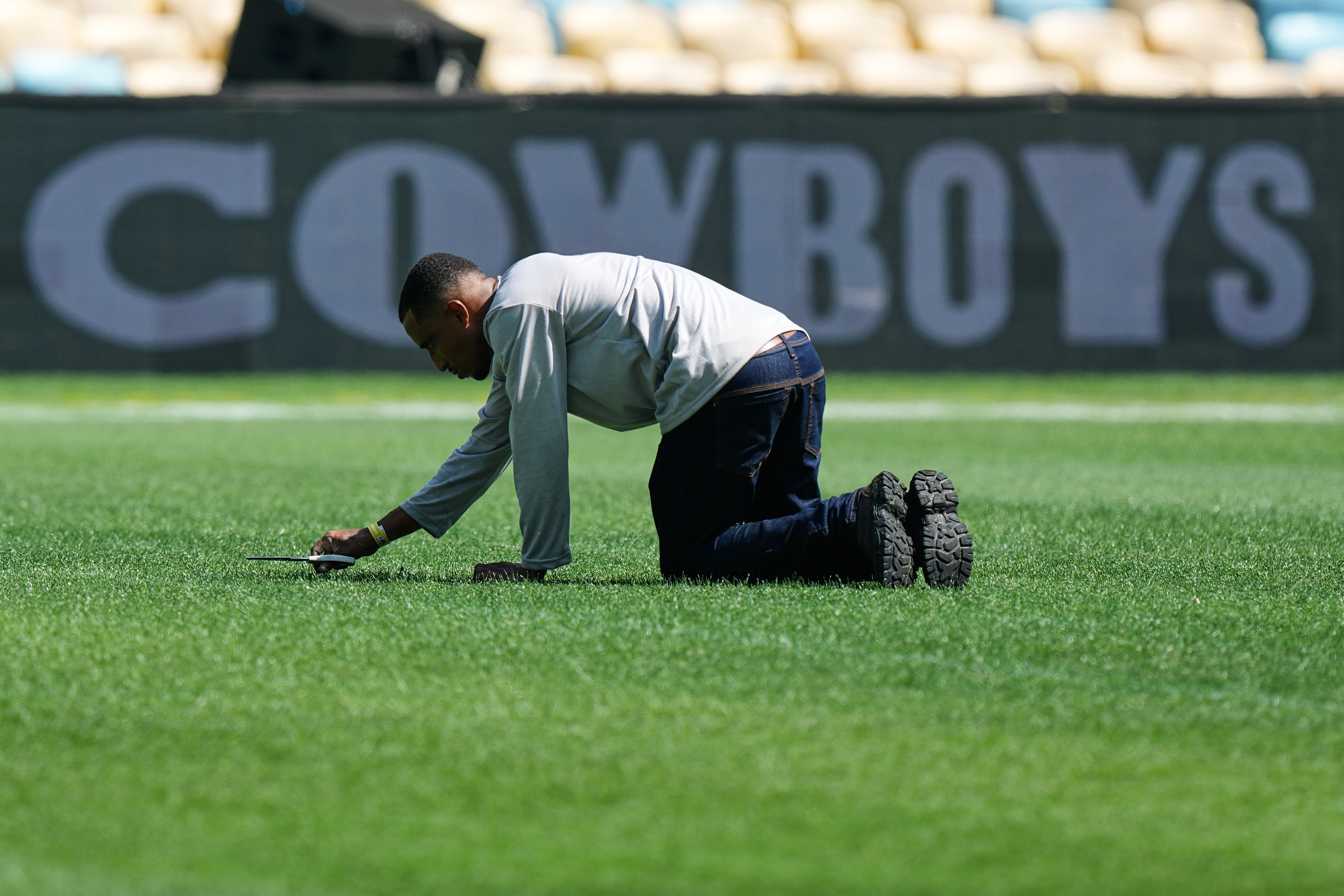 A worker cuts grass with scissors on the field ahead of an NFL football game between the Dallas Cowboys and the Baltimore Ravens in Rio de Janeiro, Saturday, Sept. 26, 2026. 