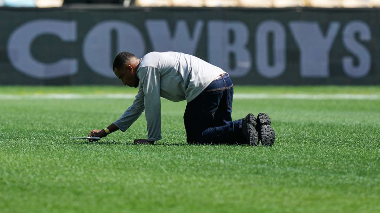 A worker cuts grass with scissors on the field ahead of an NFL football game between the Dallas Cowboys and the Baltimore Ravens in Rio de Janeiro, Saturday, Sept. 26, 2026.