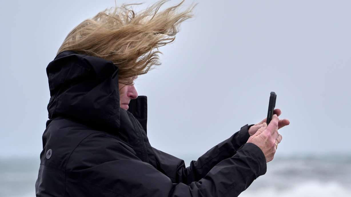 Denise Taylor of Manchester, N.H., is buffeted by the wind as she films the raging sea during a nor'easter storm in Hampton, N.H., Saturday.