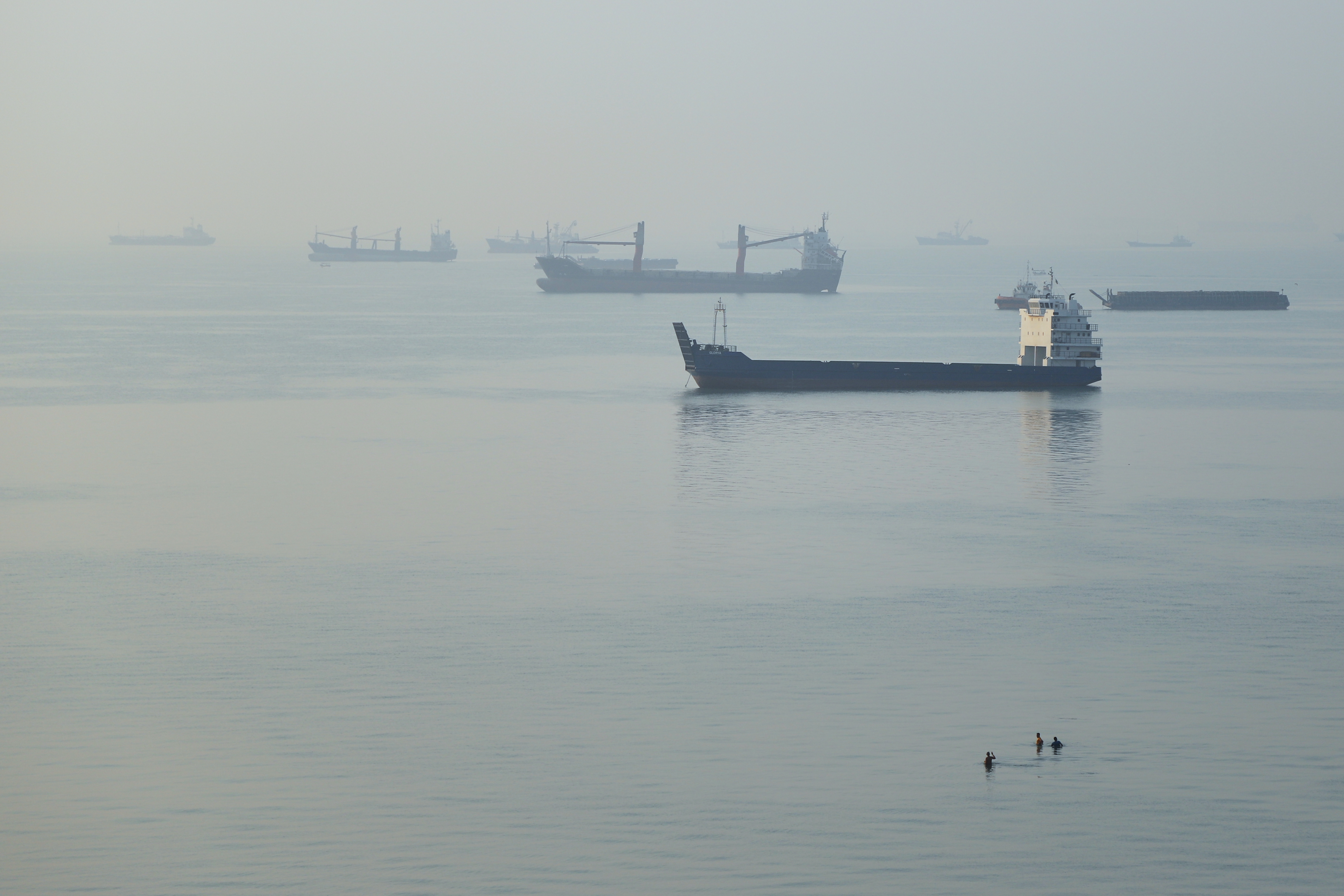 People wade in the water as cargo ships are anchored in the Strait of Hormuz off Bandar Abbas, Iran, Sept. 28. Oil prices rose on Thursday as renewed fears of a return to war in the Middle East grew.