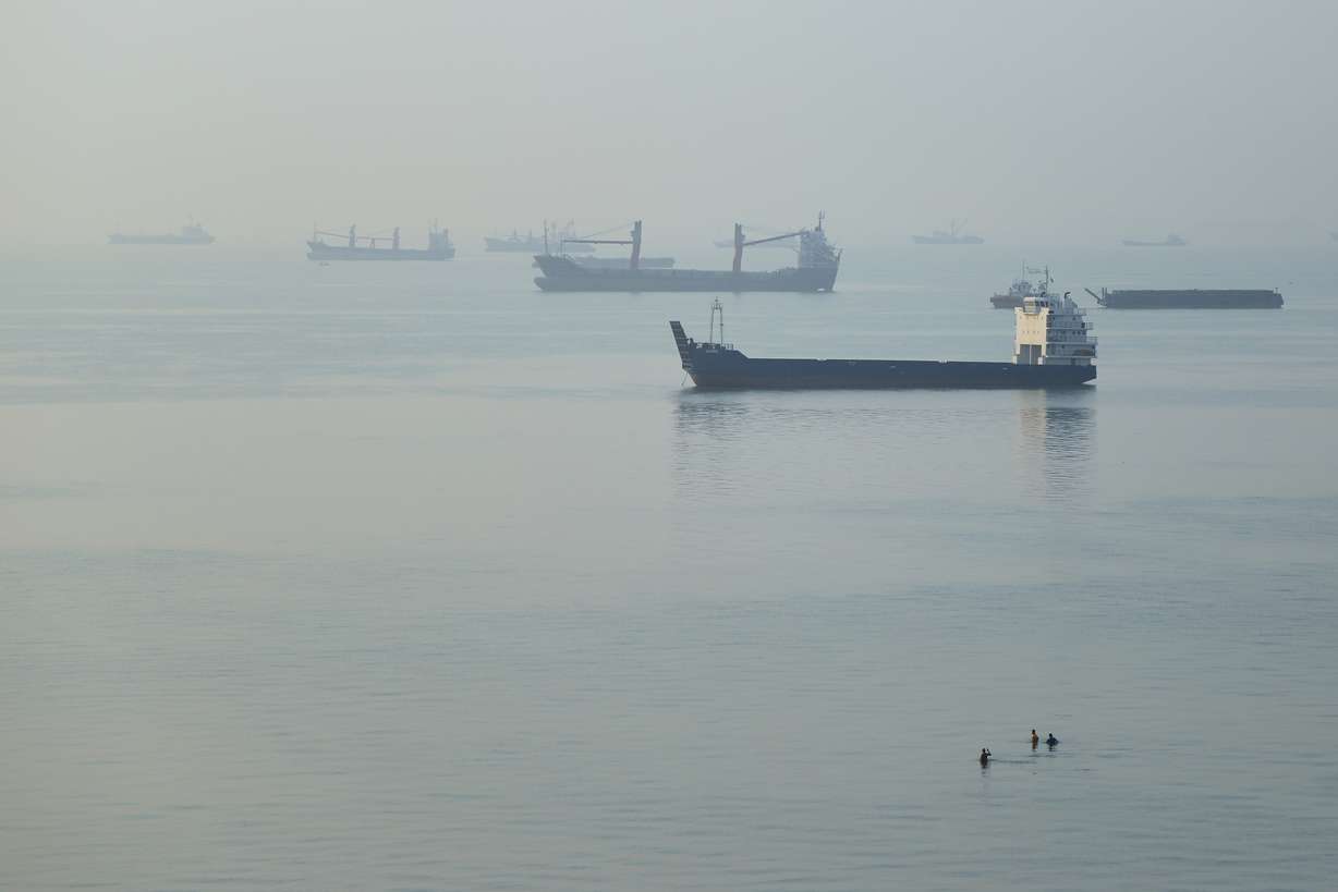 People wade in the water as cargo ships are anchored in the Strait of Hormuz off Bandar Abbas, Iran, Sept. 28. Oil prices rose on Thursday as renewed fears of a return to war in the Middle East grew.