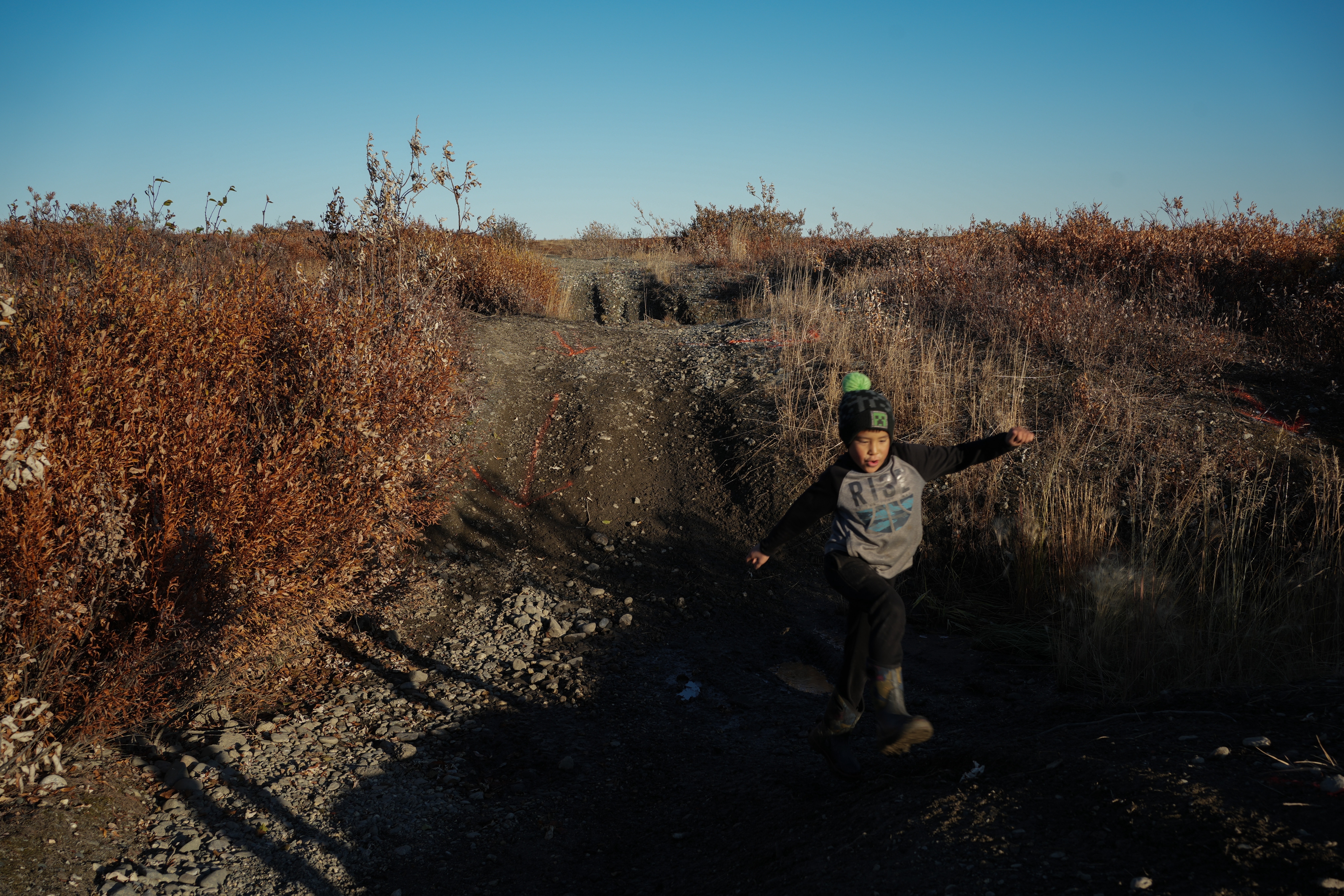James Schaeffer, 7, plays on a road where thawing permafrost has caused the ground to warp in Kotzebue, Alaska, Sept. 26, 2025.