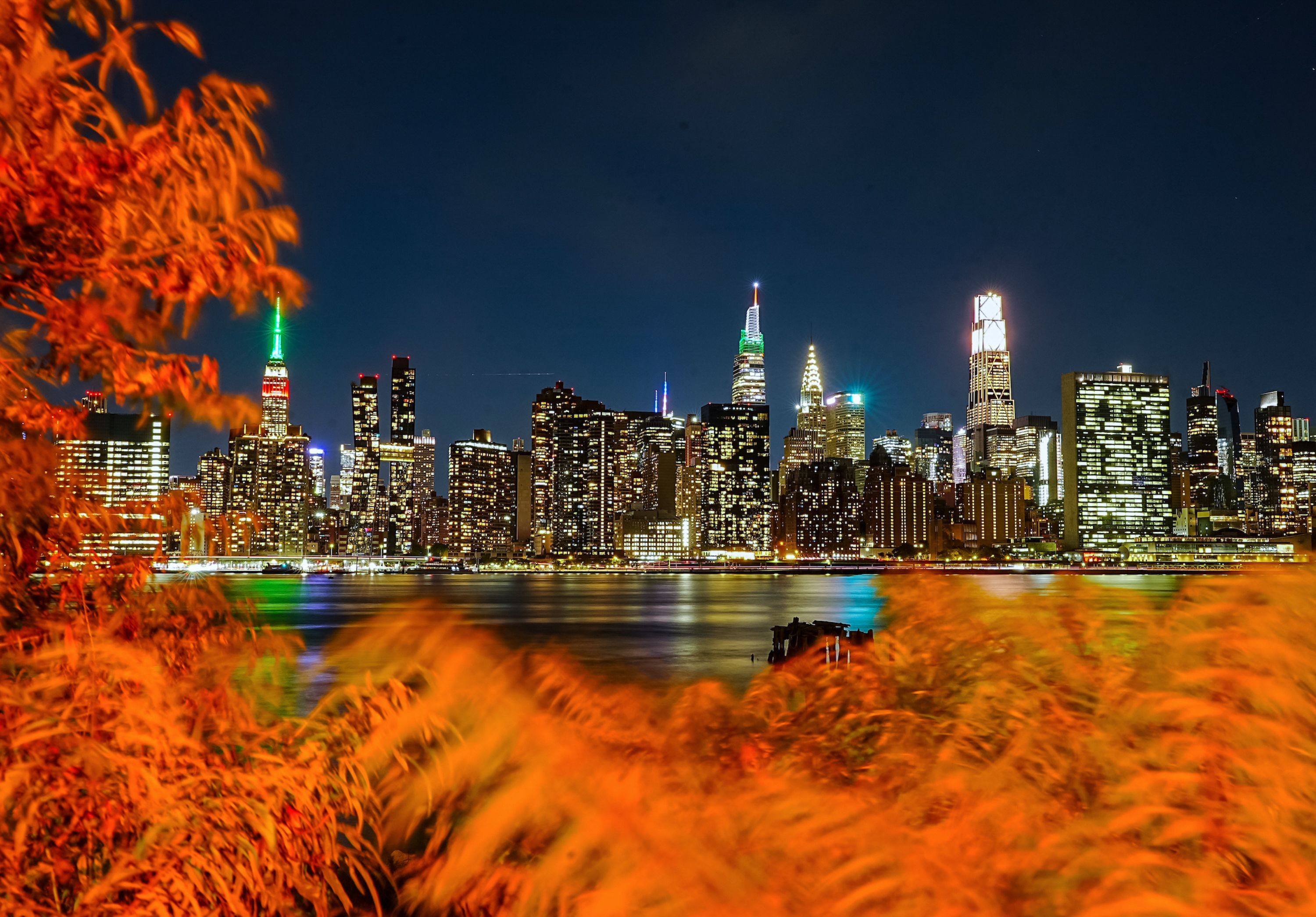 A view of the Manhattan skyline illuminated at night, with autumn foliage in the foreground along the East River in New York City, on October 12.