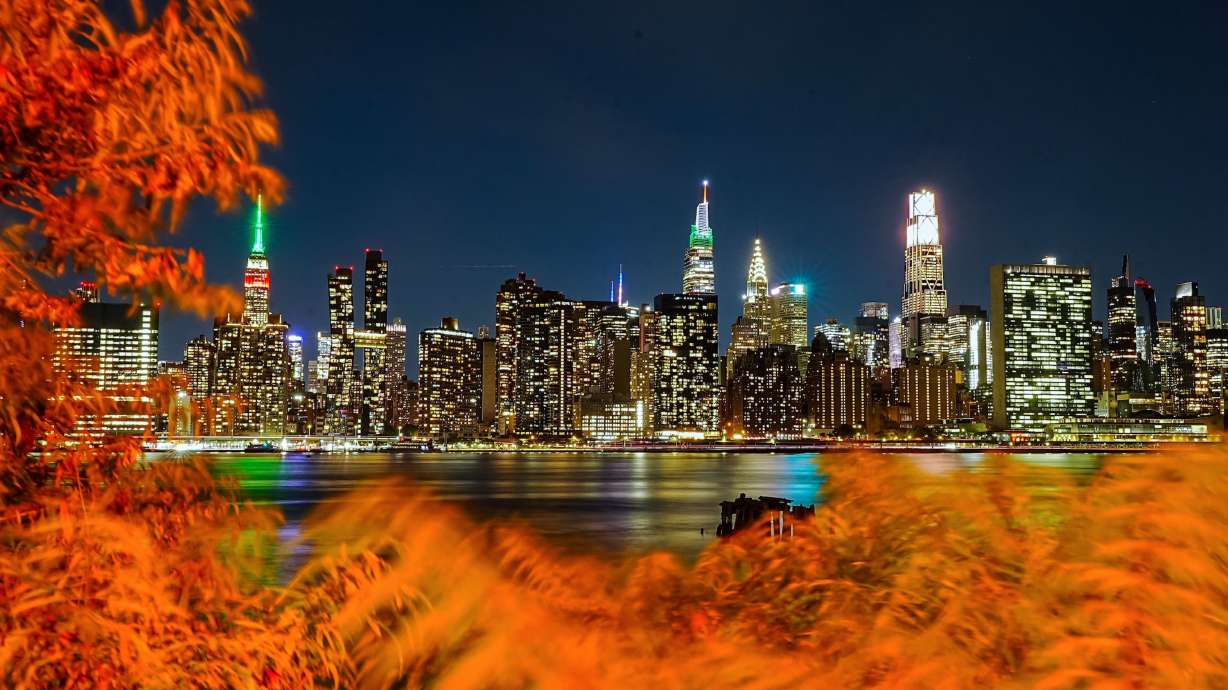 A view of the Manhattan skyline illuminated at night, with autumn foliage in the foreground along the East River in New York City, on October 12.