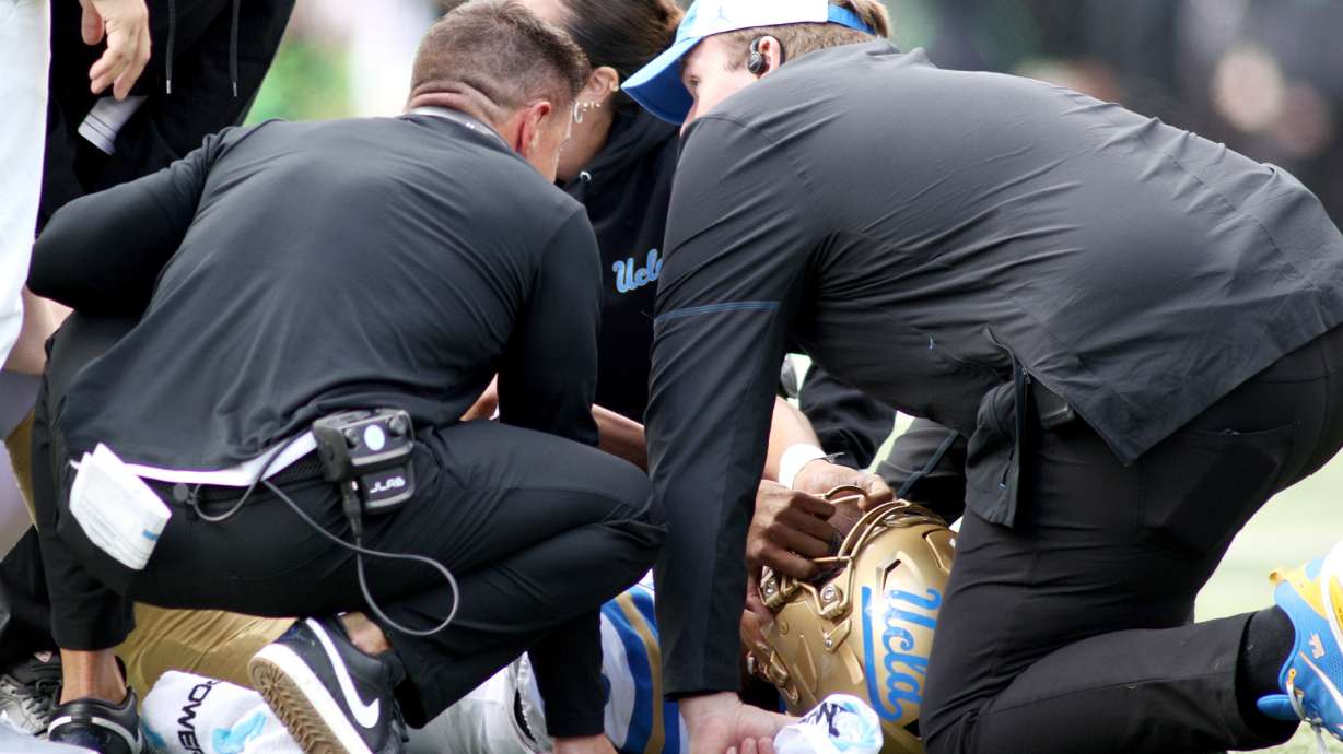 UCLA quarterback Nico Iamaleava (9) is examined by head coach Bob Chesney, left, and medical staff during the first half of an NCAA college football game against Oregon, Saturday, Oct. 10, 2026, in Eugene, Ore.
