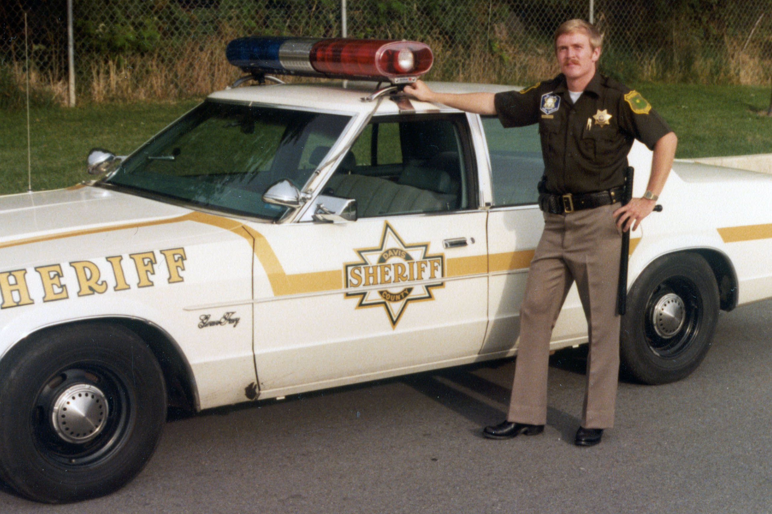 Brian Weese served as a deputy and paramedic for the Davis County Sheriff's Office during the 1980s. This image from Weese's scrapbook shows him standing alongside a sheriff's patrol car.