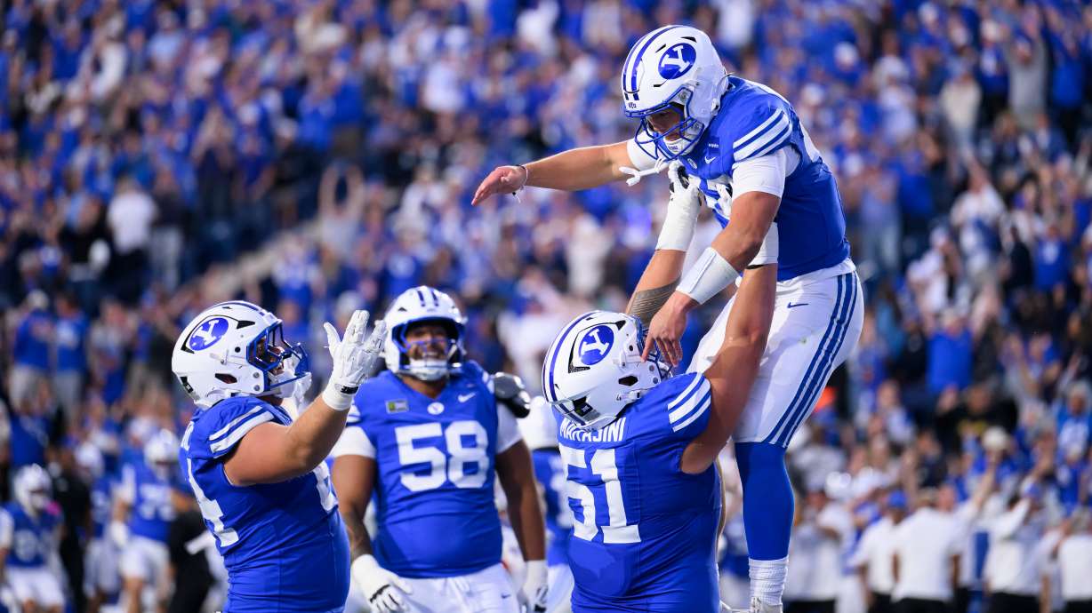 BYU offensive lineman Sonny Makasini, center right, lifts quarterback Bear Bachmeier, top, after Bachmeier ran for a touchdown during the first half of an NCAA college football game against Notre Dame, Saturday, Oct. 17, 2026, in Provo, Utah.