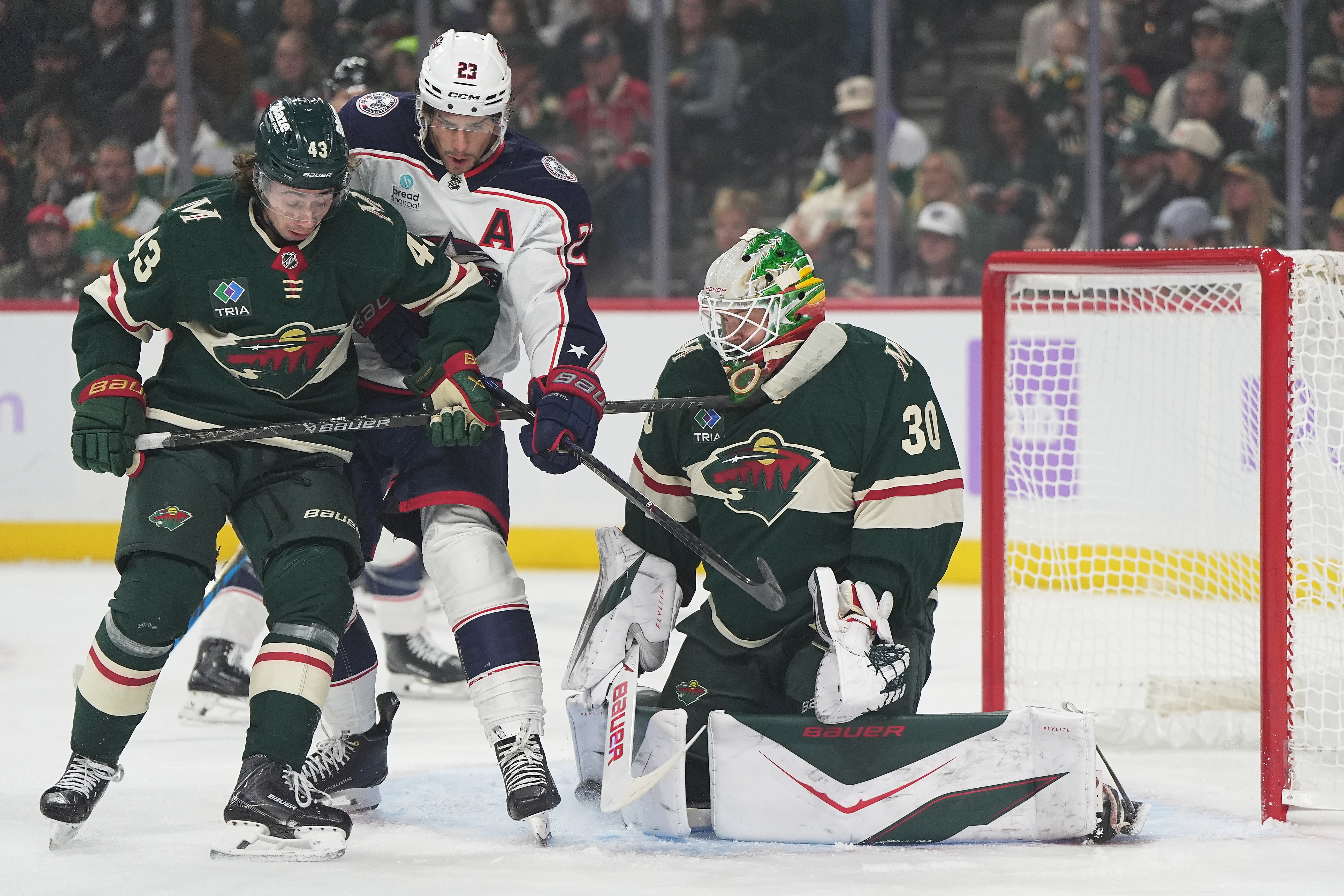 Minnesota Wild goaltender Jesper Wallstedt (30) and defenseman Quinn Hughes (43) defend against a shot as Columbus Blue Jackets center Sean Monahan (23) pressures them during the first period of an NHL hockey game, Sunday, Oct. 18, 2026, in St. Paul, Minn. 