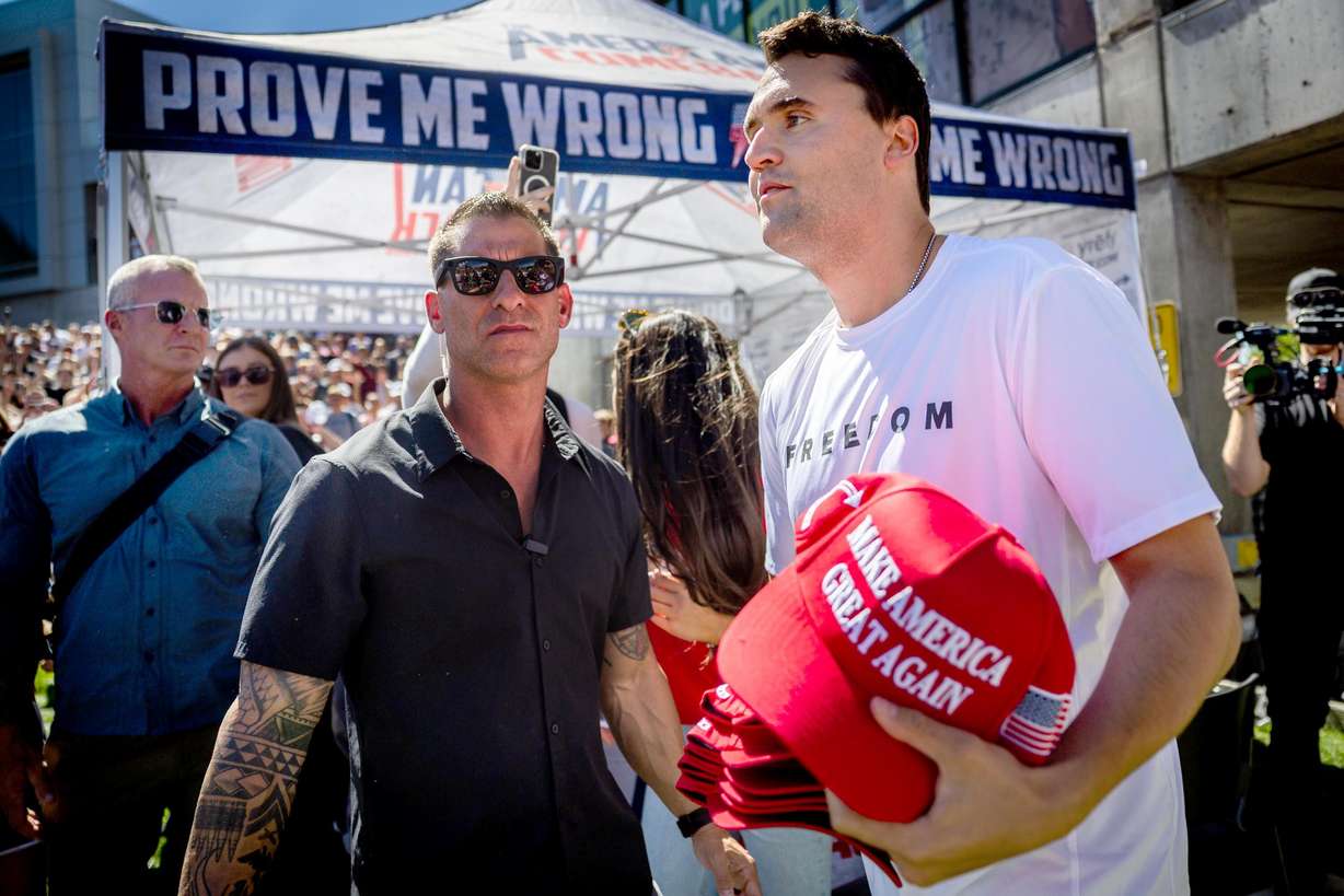 Charlie Kirk’s, the CEO and co-founder of the conservative youth organization Turning Point USA, security guards, left, stands by as Kirk hands out hats before Kirk is fatally shot during Turning Point USA’s visit to Utah Valley University in Orem on Sept. 10, 2025.