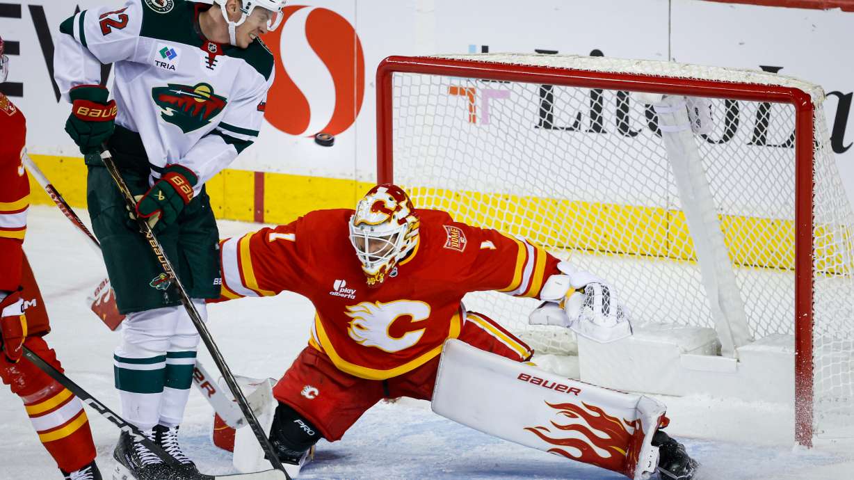 Minnesota Wild's Matt Boldy, second from right, jumps out of the way of the puck as Calgary Flames goalie Devin Cooley defends the net during the third period of an NHL hockey game in Calgary, Alberta, Thursday, Oct. 22, 2026.