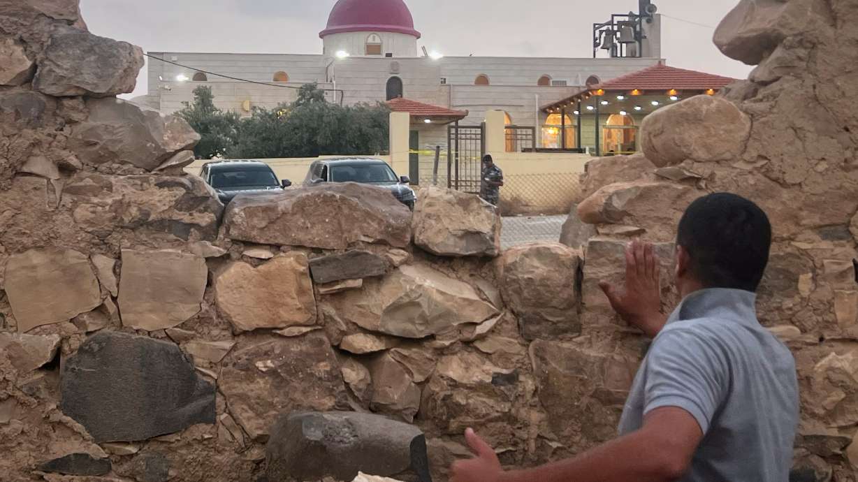 A man looks through a gap in a stone wall toward a Greek Orthodox church where gunmen opened fire during a funeral hours earlier in Hamoud village, in Jordan's Karak governorate, Friday.