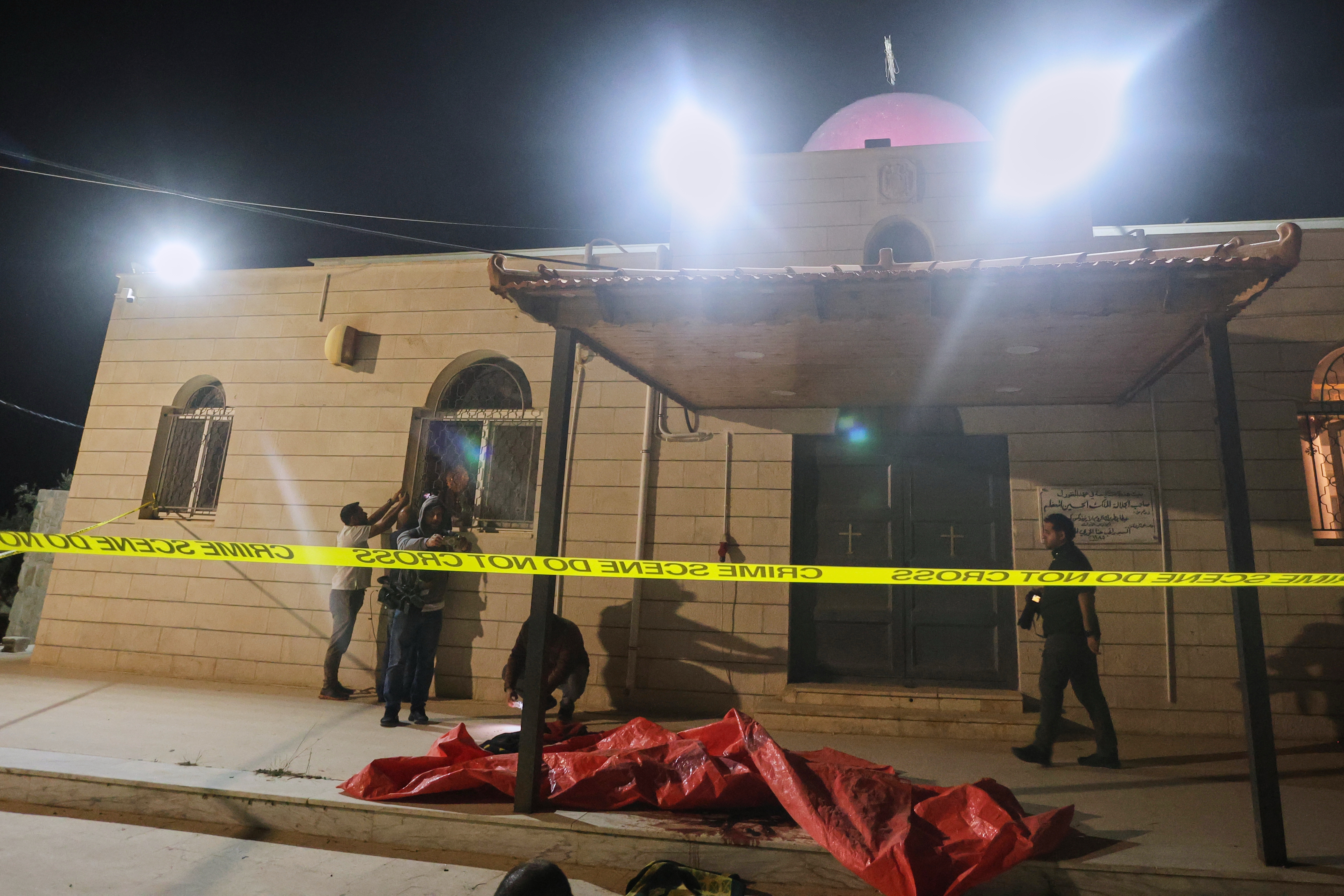 Journalists and other people stand outside a Greek Orthodox church cordoned off with crime scene tape hours after gunmen opened fire during a funeral in Hamoud village, in Jordan's Karak governorate, Friday.