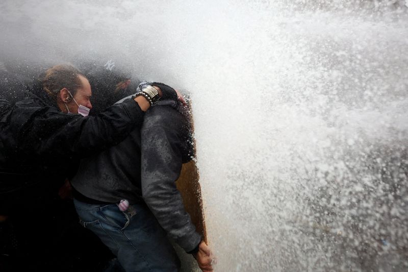 Protesters take cover behind a plywood board as French riot police use a water canon amid clashes during nationwide protests against the cost of living and rising fuel prices, in France, Saturday. The clashes resulted in nearly 1,000 arrests.