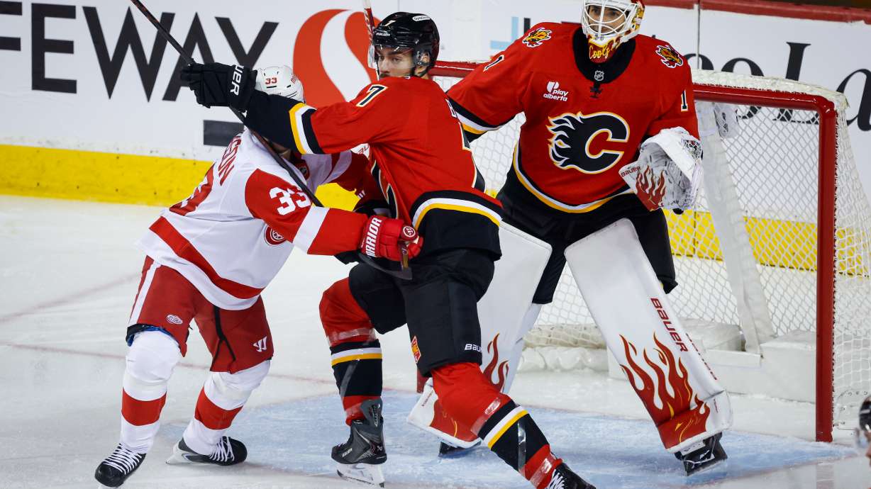 Detroit Red Wings' Viktor Arvidsson, left, is checked by Calgary Flames' Kevin Bahl, center, as goalie Devin Cooley follows the play during the first period of an NHL hockey game in Calgary, Alberta, Saturday, Oct. 24, 2026.