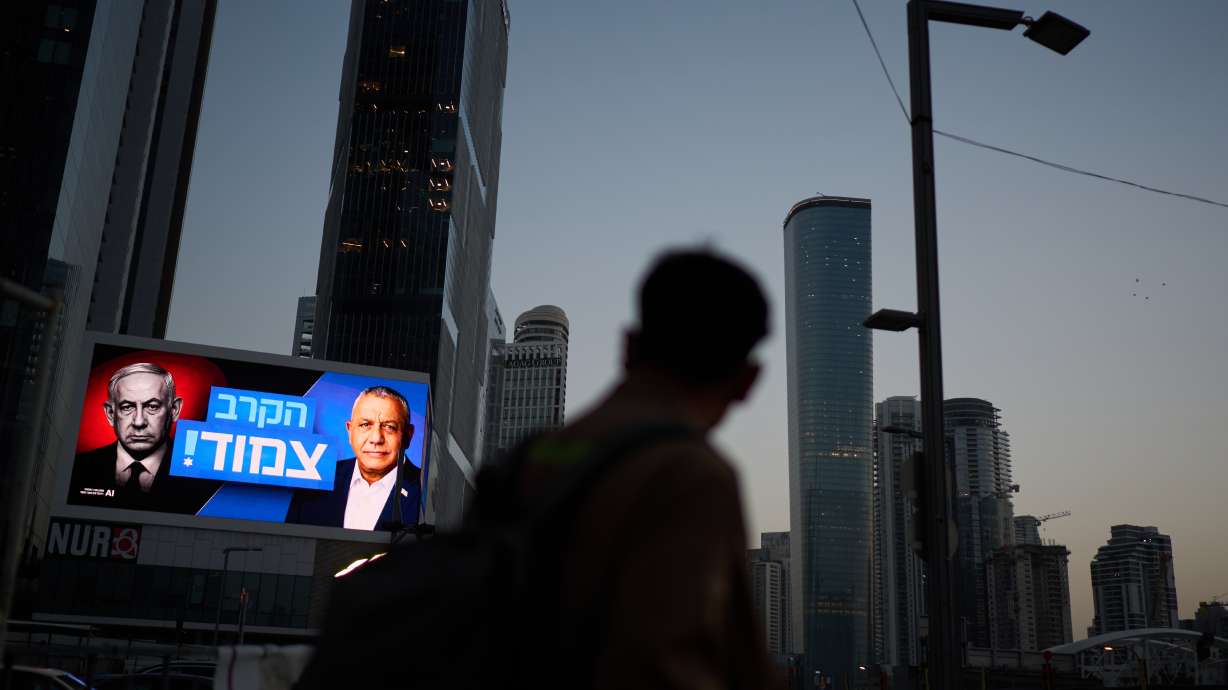 A pedestrian passes a campaign billboard featuring Israeli Prime Minister Benjamin Netanyahu and his main rival, opposition candidate Gadi Eisenkot, with a message in Hebrew that reads "The race is tight," Friday, in Tel Aviv. Netanyahu, who cast his vote early on Tuesday, called it a "very moving and fateful moment."