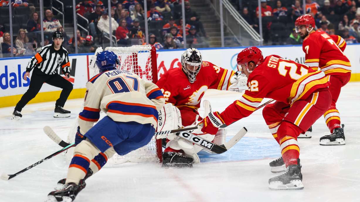 Edmonton Oilers' Connor McDavid, left, looks for an opportunity against Calgary Flames goaltender Dustin Wolf, center, during the second period of an NHL hockey game in Edmonton, Alberta, Wednesday, Oct. 28, 2026.