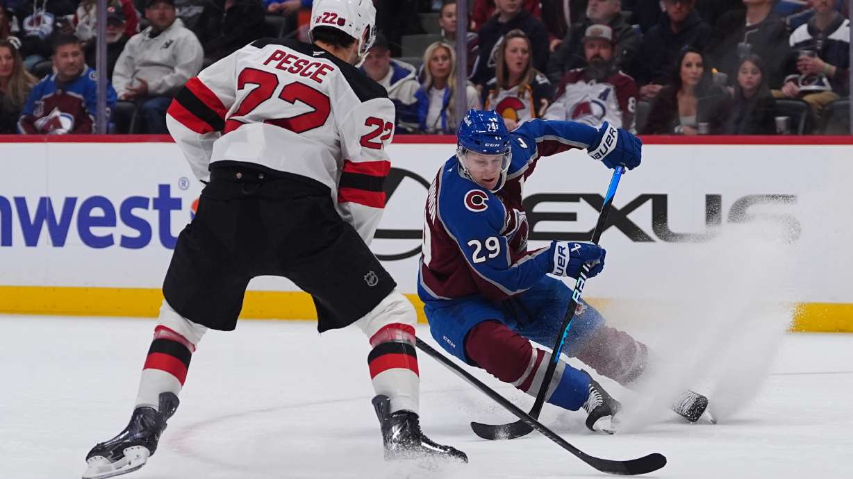 Colorado Avalanche center Nathan MacKinnon, right, looks to pass the puck as New Jersey Devils defenseman Brett Pesce covers in the first period of an NHL hockey game Wednesday, Oct. 28, 2026, in Denver.
