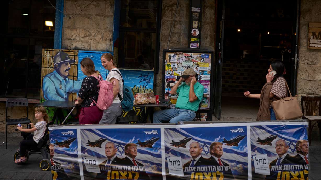 People walk next to a Likud party campaign ad featuring Israeli Prime Minister Benjamin Netanyahu and President Donald Trump in Jerusalem on Wednesday, a day after the elections in Israel. Final results are expected on Thursday.