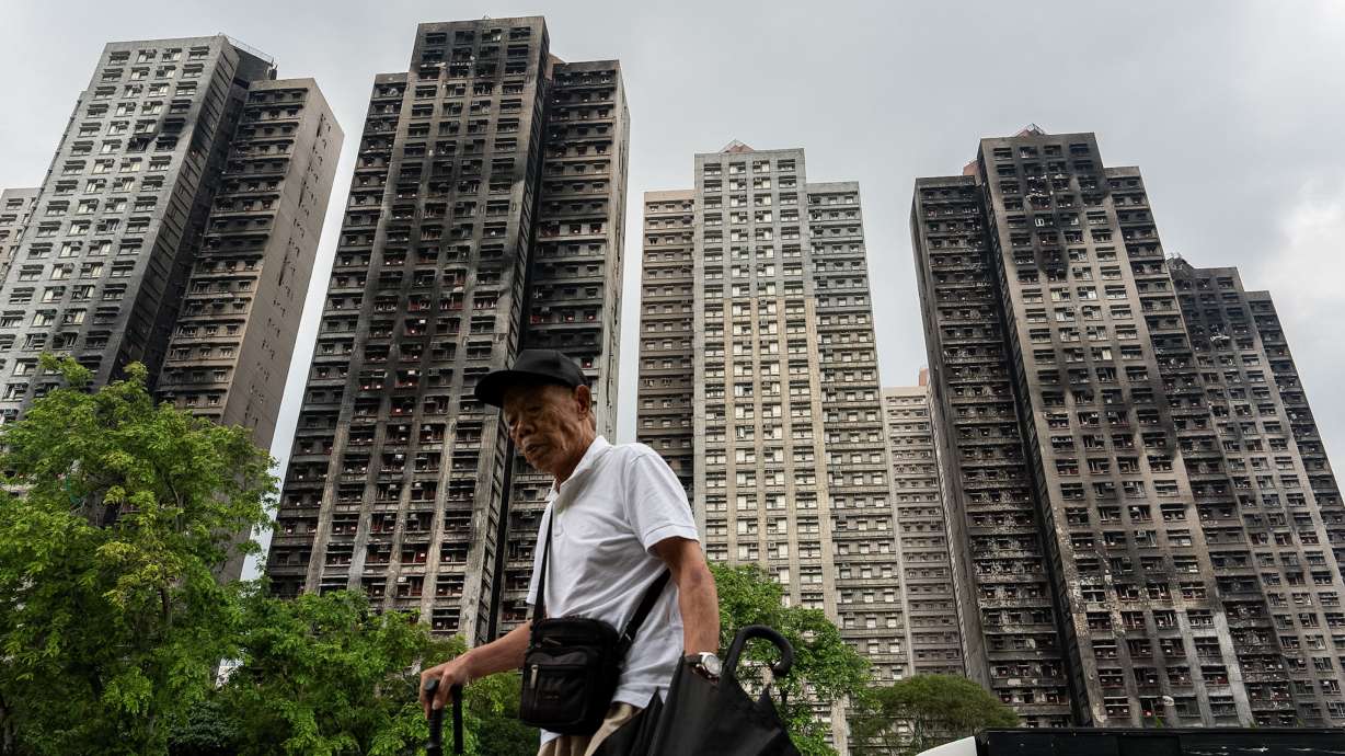 A person walks past fire-ravaged residential towers of the Wang Fuk Court apartment complex after the deadly fire in November, in the Tai Po district of Hong Kong, April 20. The country's housing secretary resigned over the fire on Thursday.