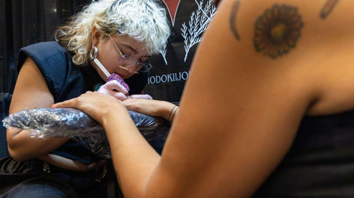 This photo provided by KOSU shows Hodokii Johnson, Muscogee and descendant of the Cheyenne and Arapaho Tribes, holding the hand of Kristin Gentry, Choctaw, as they hand poke three brown lines on each finger on Saturday, Oct. 24 Oklahoma City.